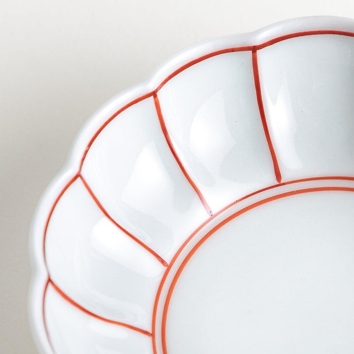 A small white porcelain dessert bowl with delicate blue or red lines radiating from the center, creating a simple yet elegant design.