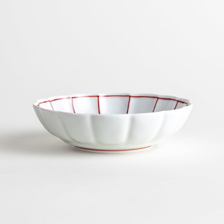 A small white porcelain dessert bowl with delicate blue or red lines radiating from the center, creating a simple yet elegant design.