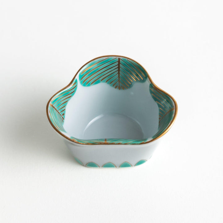 A small, white ceramic bowl with a green fan-like pattern and gold trim.