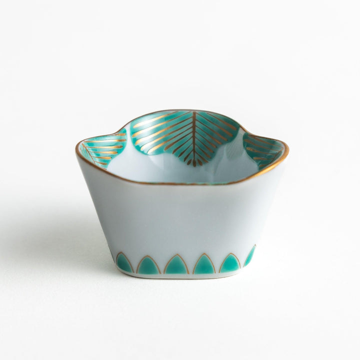 A small, white ceramic bowl with a green fan-like pattern and gold trim.