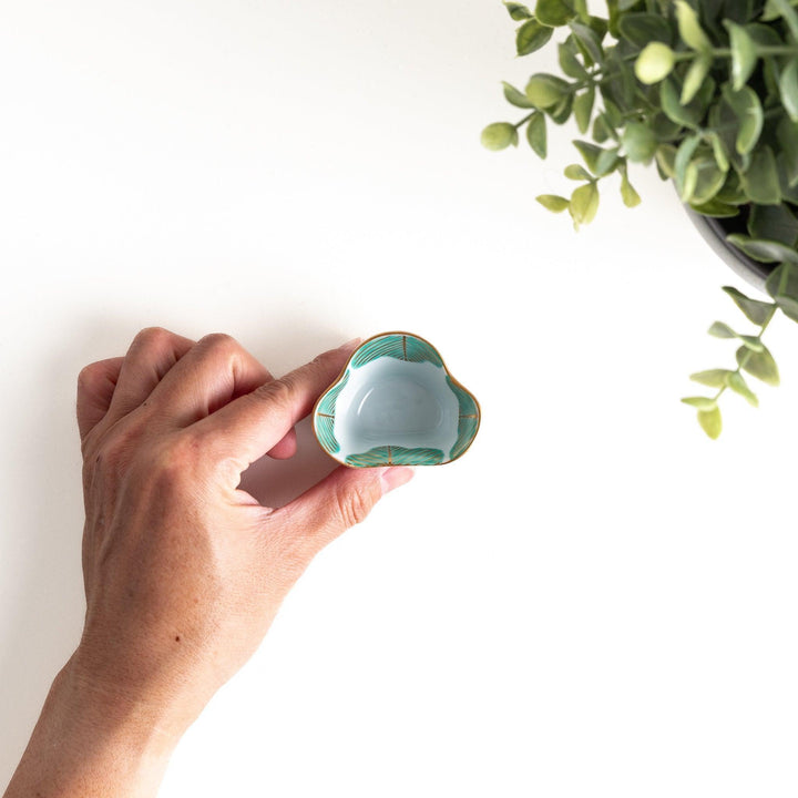 A small, white ceramic bowl with a green fan-like pattern and gold trim.