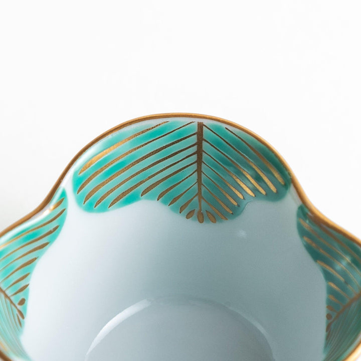 A small, white ceramic bowl with a green fan-like pattern and gold trim.