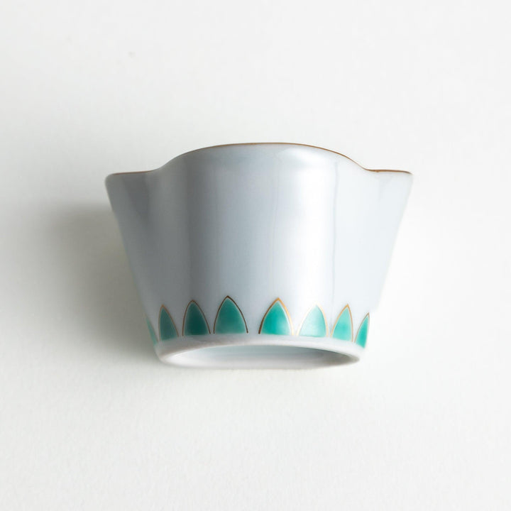 A small, white ceramic bowl with a green fan-like pattern and gold trim.