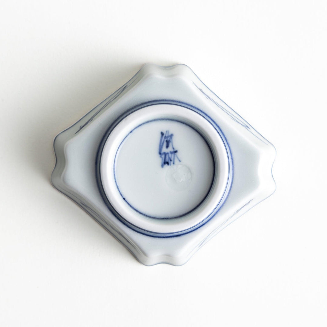 A small square dish with a blue and white design, featuring blue brushstroke patterns and a silver spoon next to it.