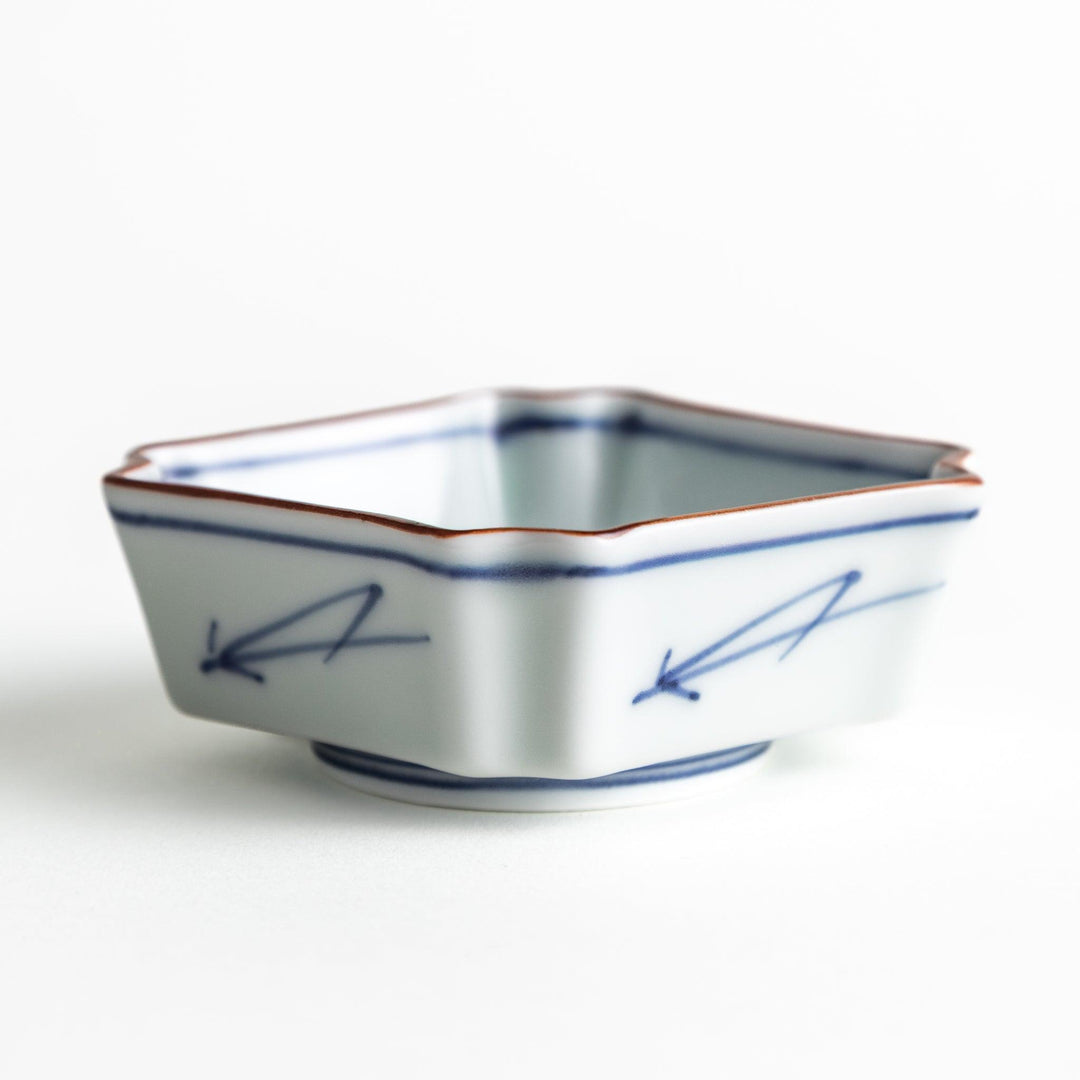 A small square dish with a blue and white design, featuring blue brushstroke patterns and a silver spoon next to it.