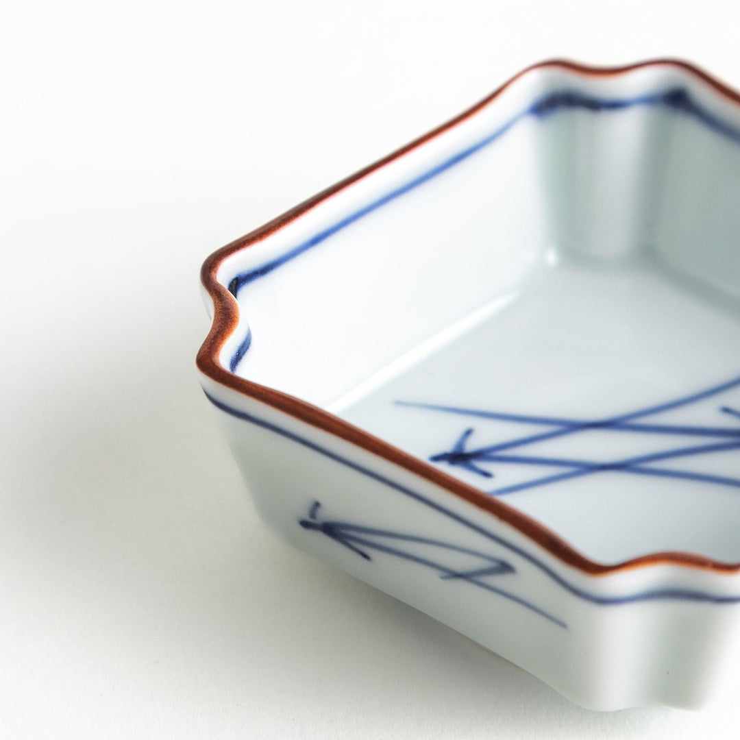 A small square dish with a blue and white design, featuring blue brushstroke patterns and a silver spoon next to it.