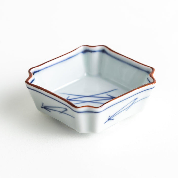 A small square dish with a blue and white design, featuring blue brushstroke patterns and a silver spoon next to it.