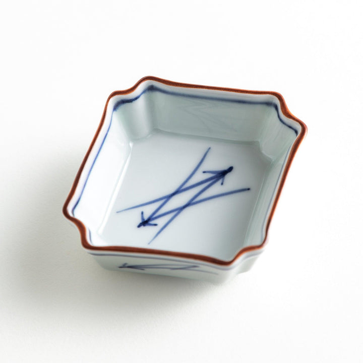 A small square dish with a blue and white design, featuring blue brushstroke patterns and a silver spoon next to it.