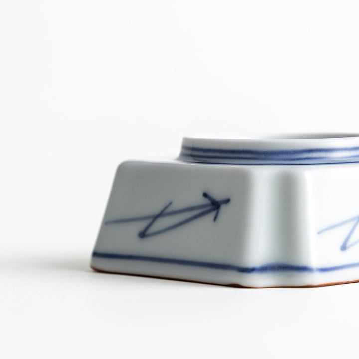 A small square dish with a blue and white design, featuring blue brushstroke patterns and a silver spoon next to it.