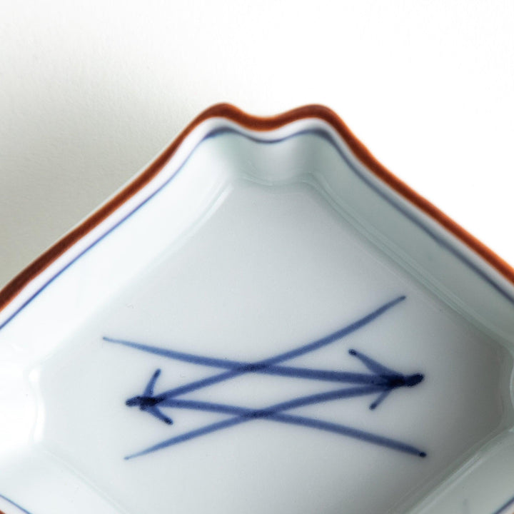 A small square dish with a blue and white design, featuring blue brushstroke patterns and a silver spoon next to it.