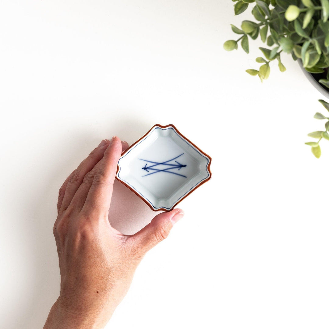 A small square dish with a blue and white design, featuring blue brushstroke patterns and a silver spoon next to it.