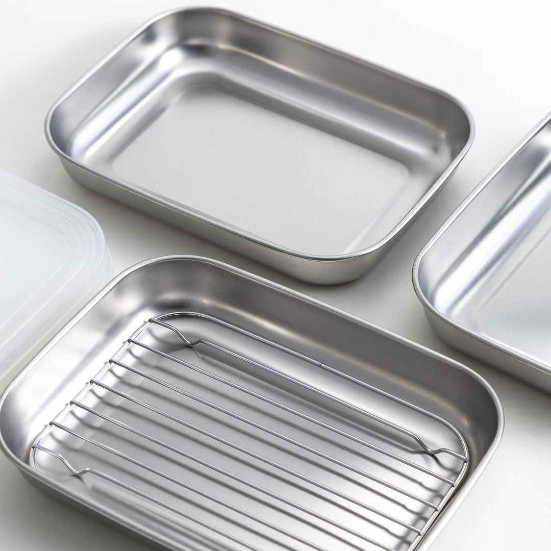 Rectangular stainless steel food prep trays with a wire rack and a white plastic lid.