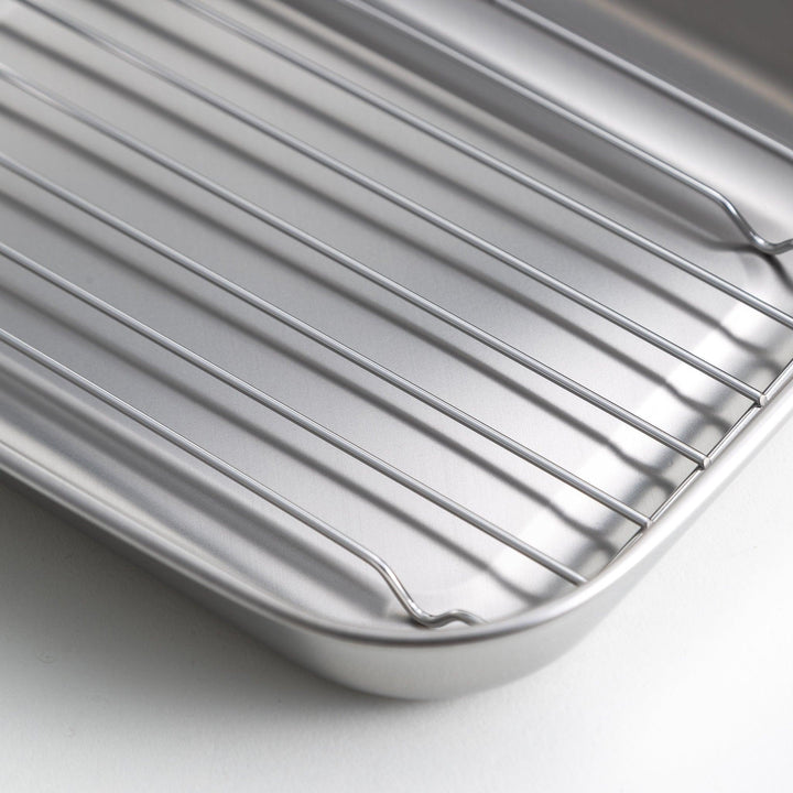 Rectangular stainless steel food prep trays with a wire rack and a white plastic lid.