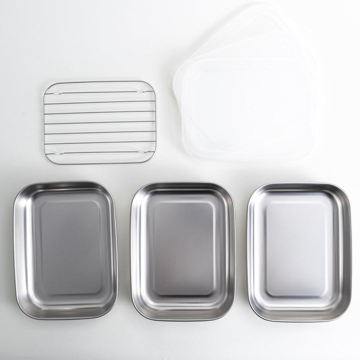 Rectangular stainless steel food prep trays with a wire rack and a white plastic lid.