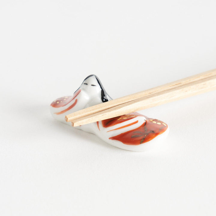 A ceramic chopstick rest shaped like a Japanese princess, painted in orange with floral accents.