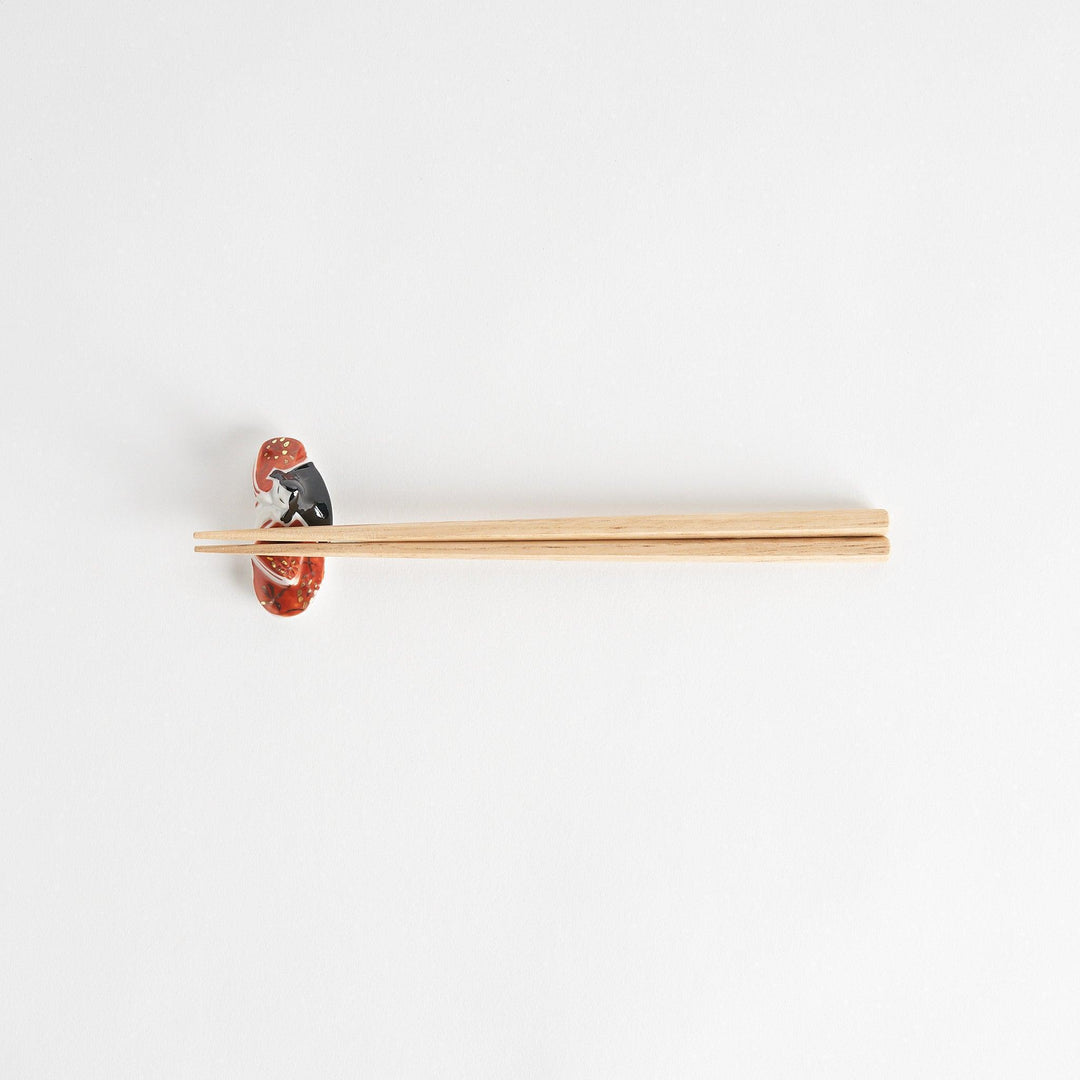 A ceramic chopstick rest shaped like a Japanese princess, painted in orange with floral accents.