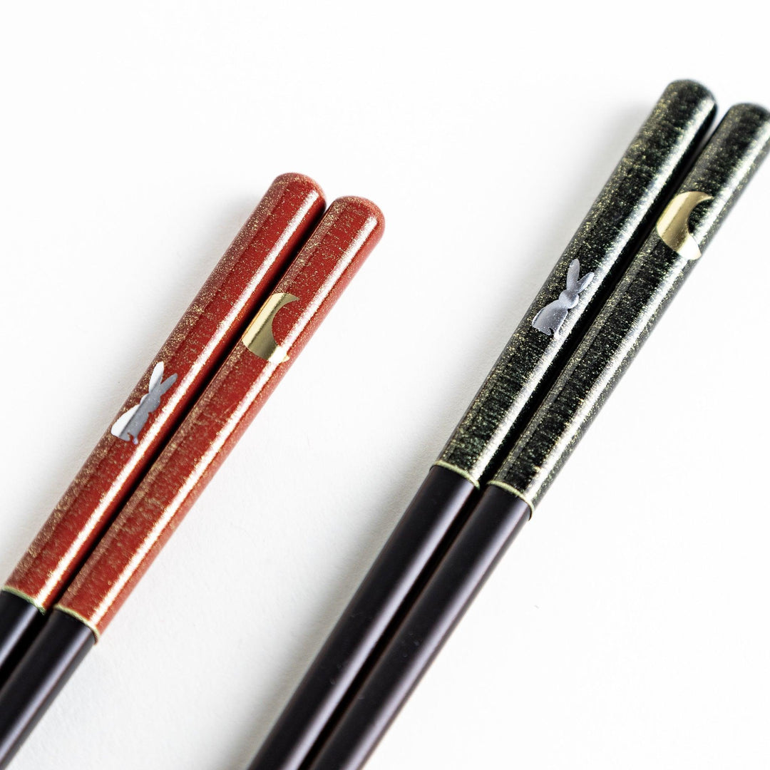 A boxed set of two pairs of chopsticks, one with a green and one with a red pattern on the handles with rabbit and moon pattern.