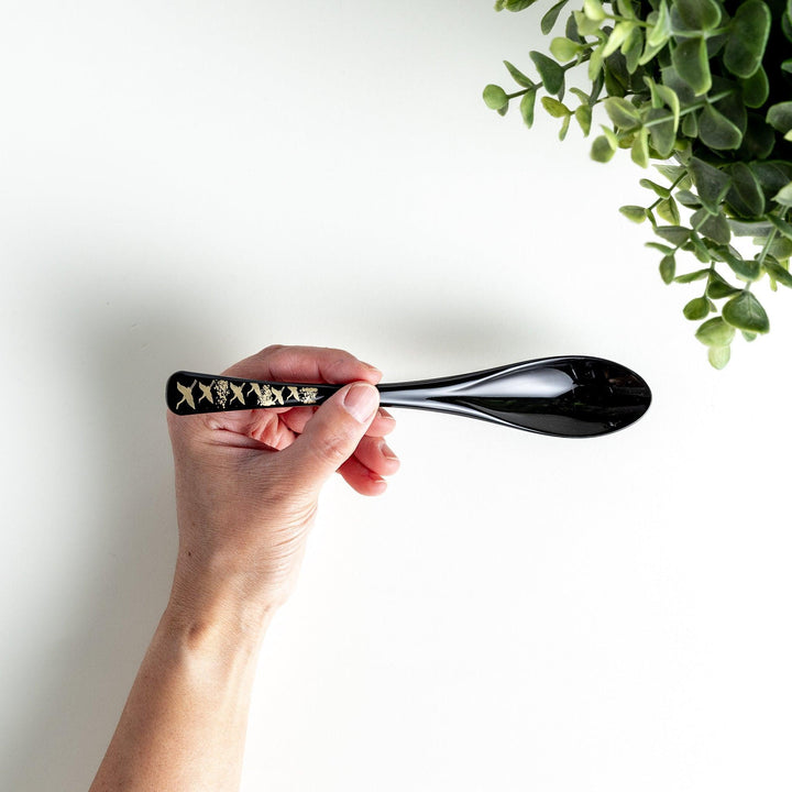 A boxed set of two lacquered spoons, one red and one black, featuring a crane pattern in gold on the handles.