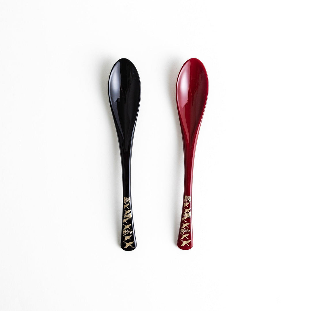 A boxed set of two lacquered spoons, one red and one black, featuring a crane pattern in gold on the handles.