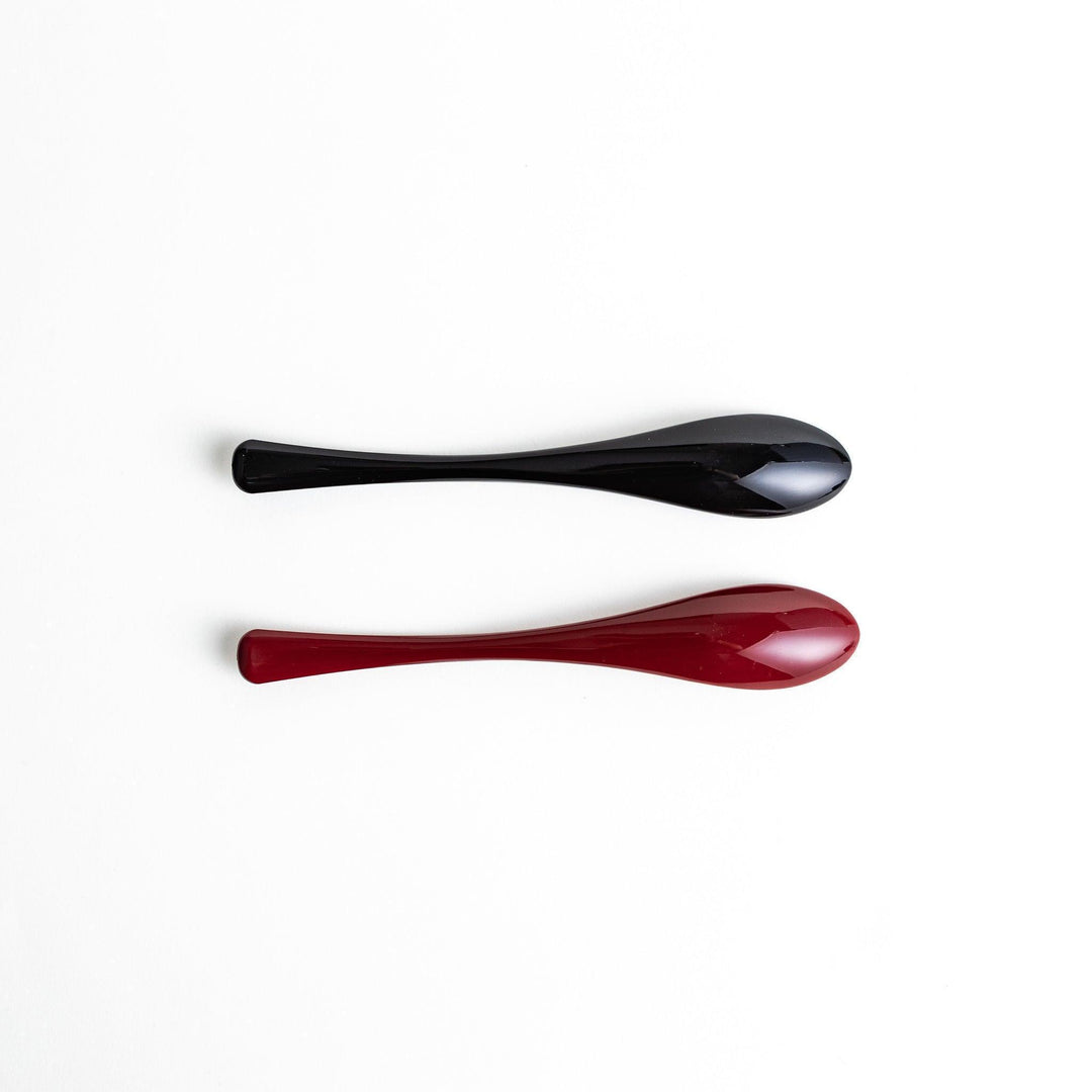 A boxed set of two lacquered spoons, one red and one black, featuring a crane pattern in gold on the handles.