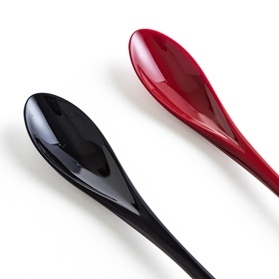 A boxed set of two lacquered spoons, one red and one black, featuring a crane pattern in gold on the handles.