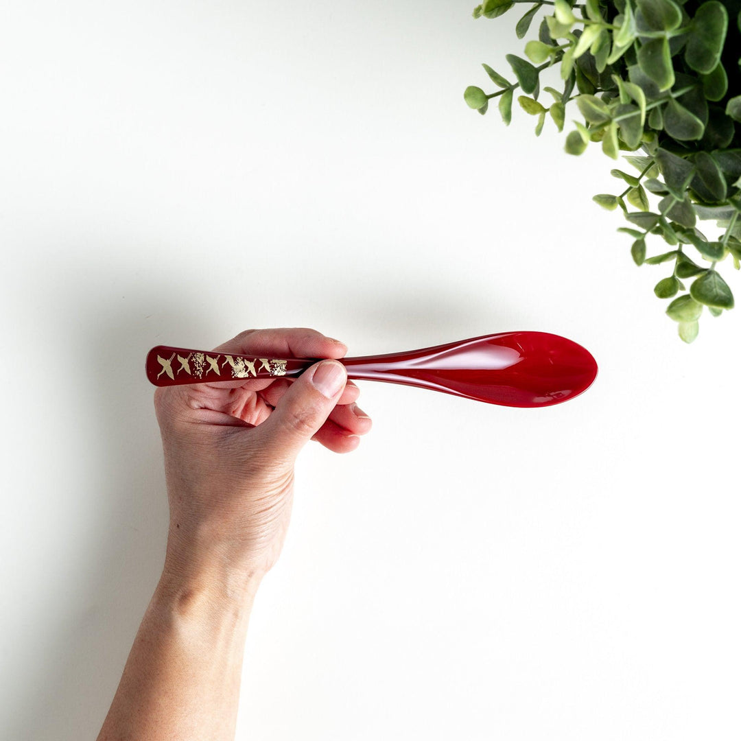 A boxed set of two lacquered spoons, one red and one black, featuring a crane pattern in gold on the handles.