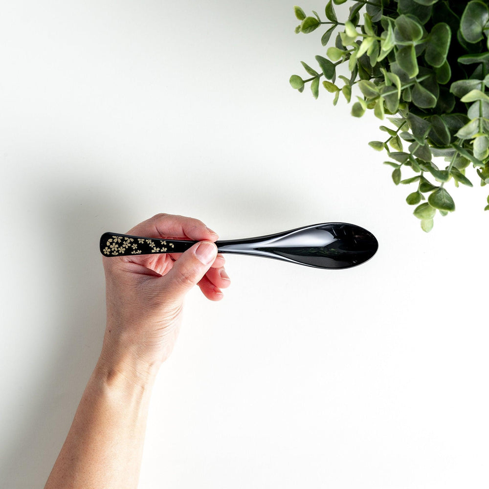 A boxed set of two lacquered spoons, one red and one black, each with gold sakura patterns on the handles.