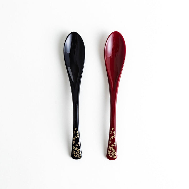 A boxed set of two lacquered spoons, one red and one black, each with gold sakura patterns on the handles.