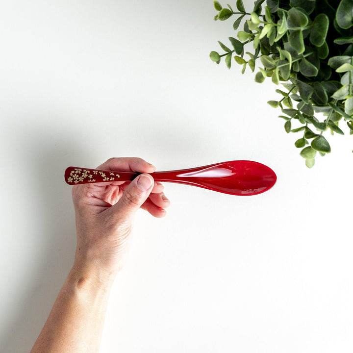 A boxed set of two lacquered spoons, one red and one black, each with gold sakura patterns on the handles.