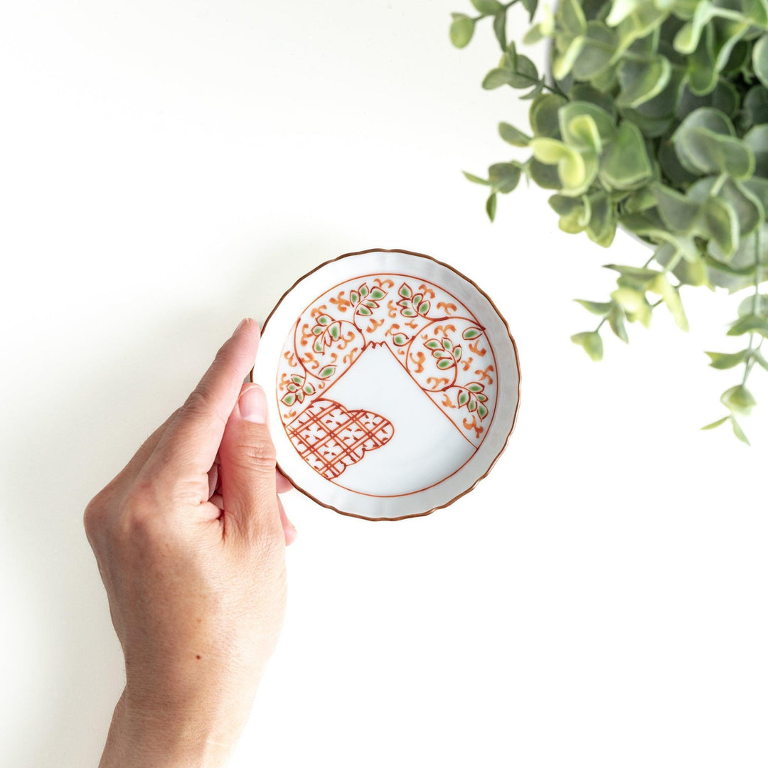 A ceramic plate decorated with an orange and green floral motif, with Mount Fuji in the center, bordered by a gold rim.