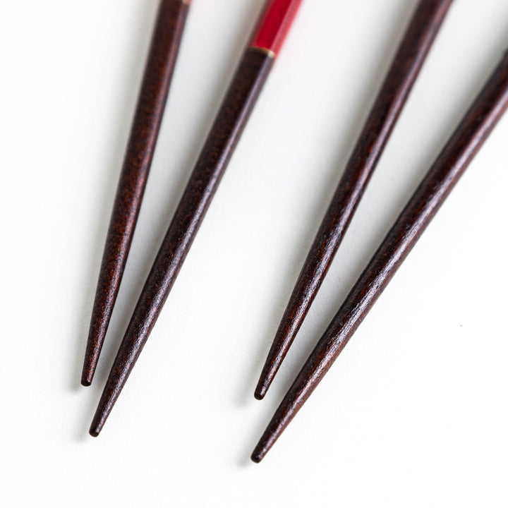 A boxed set of two pairs of chopsticks, one with black and one with red handles, both featuring textured grips.