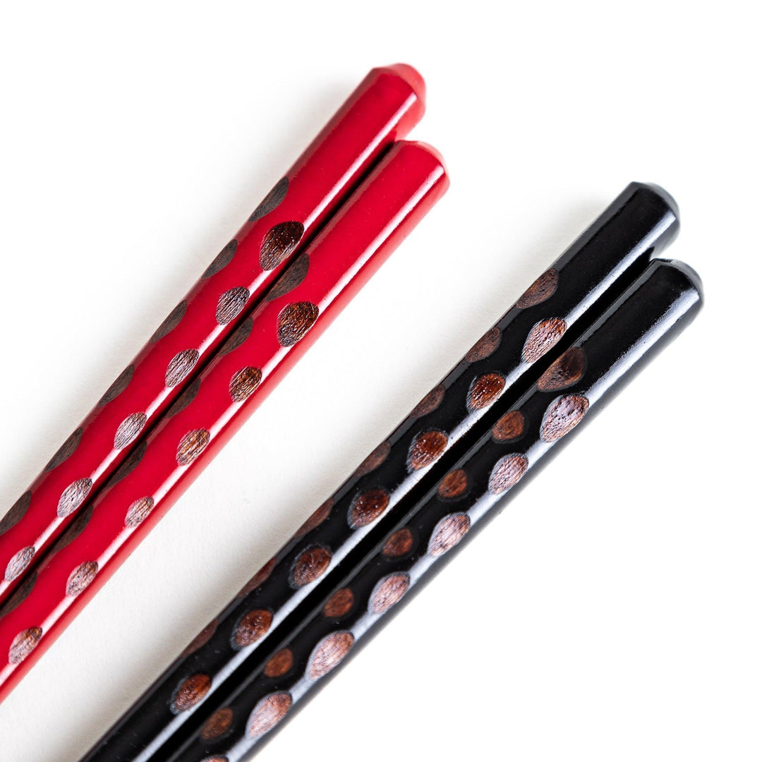 A boxed set of two pairs of chopsticks, one with black and one with red handles, both featuring textured grips.