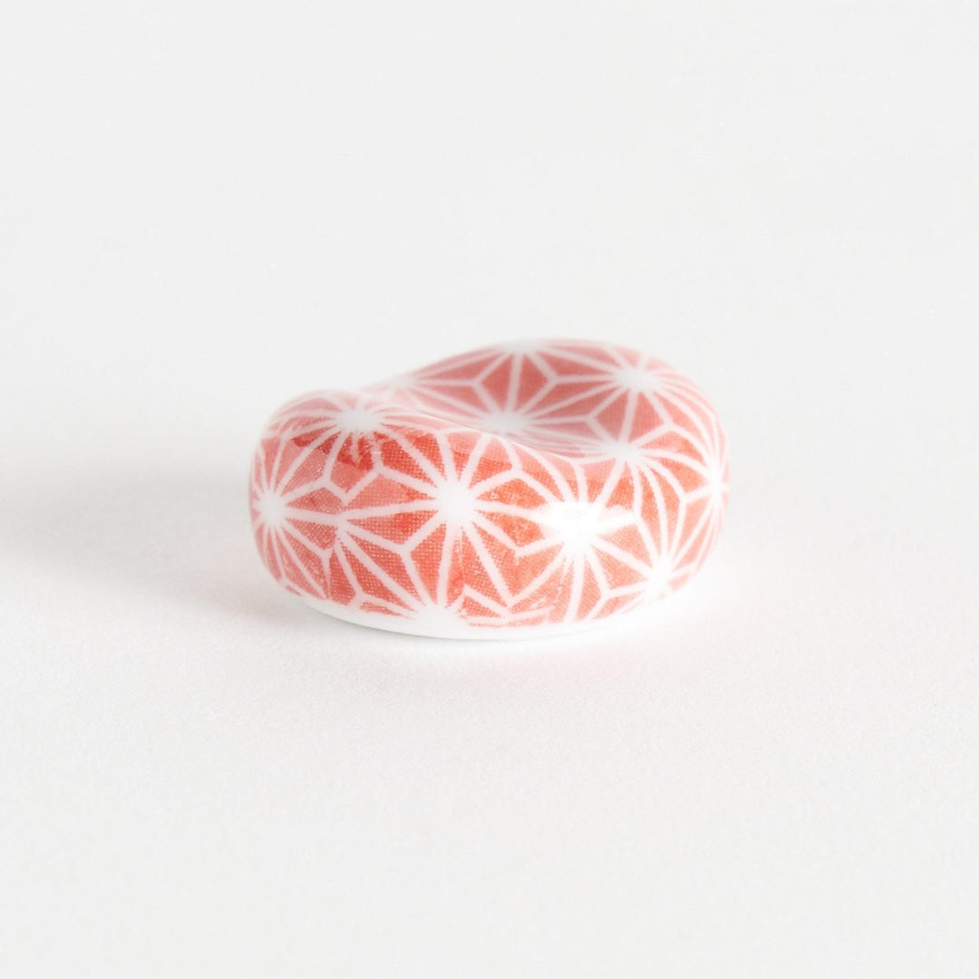 A red and white rounded ceramic chopstick rest with a starburst pattern.