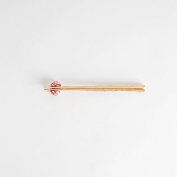 A red and white rounded ceramic chopstick rest with a starburst pattern.