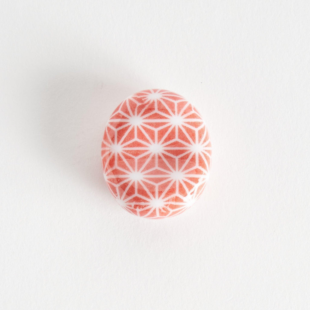 A red and white rounded ceramic chopstick rest with a starburst pattern.