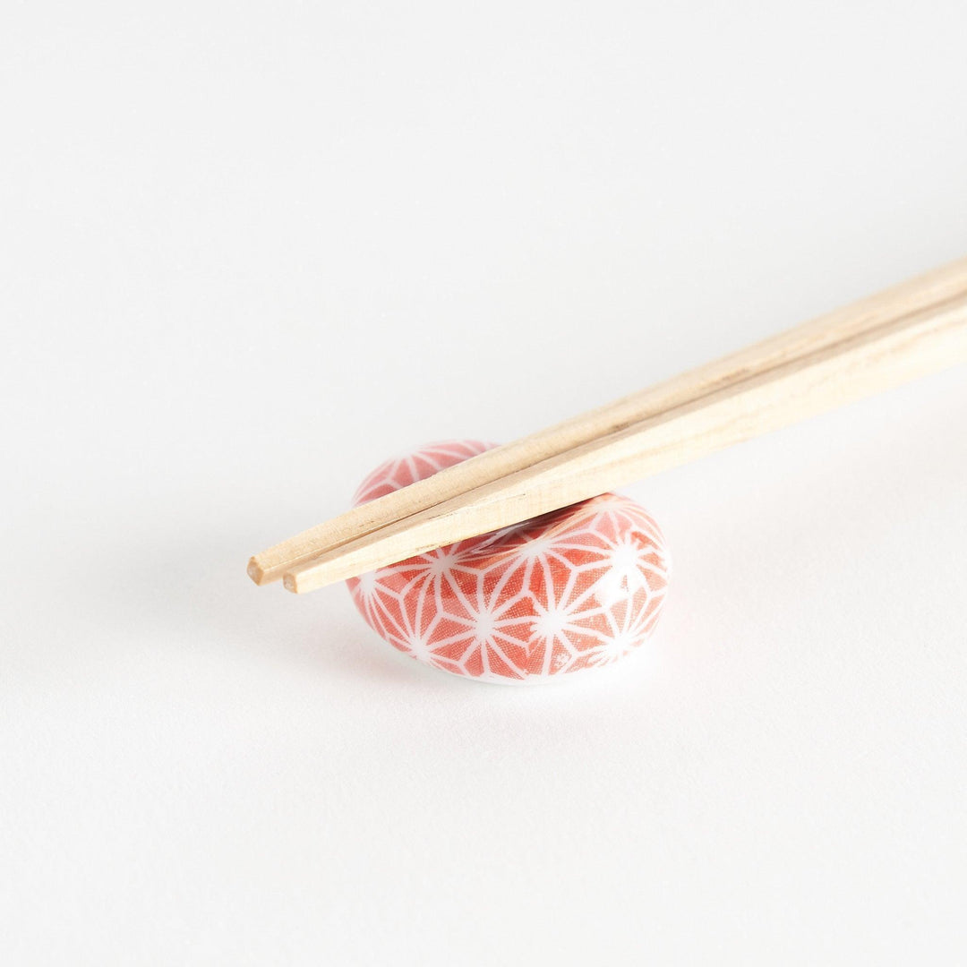 A red and white rounded ceramic chopstick rest with a starburst pattern.