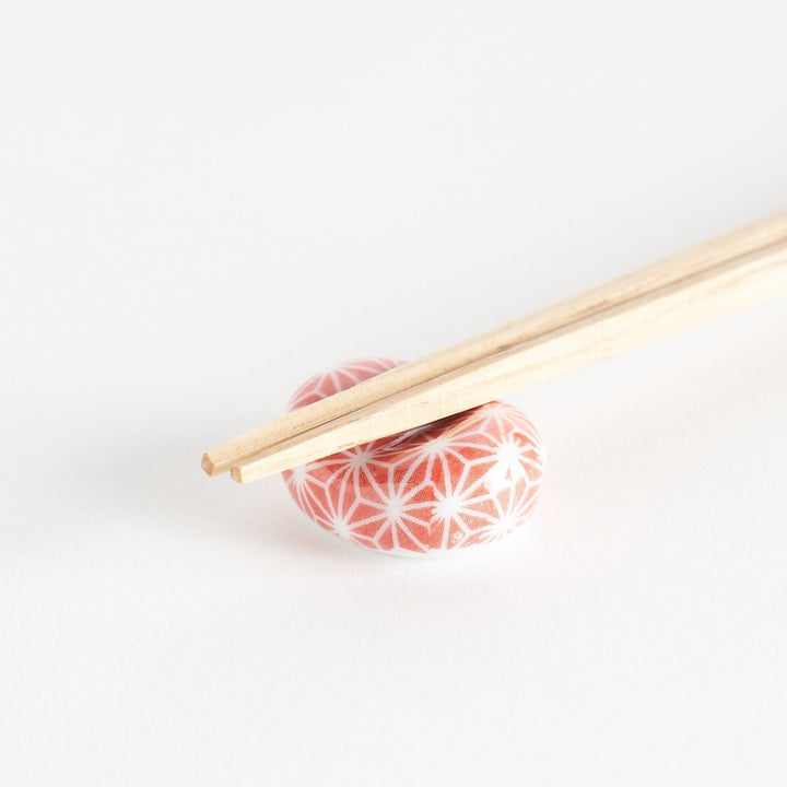 A red and white rounded ceramic chopstick rest with a starburst pattern.