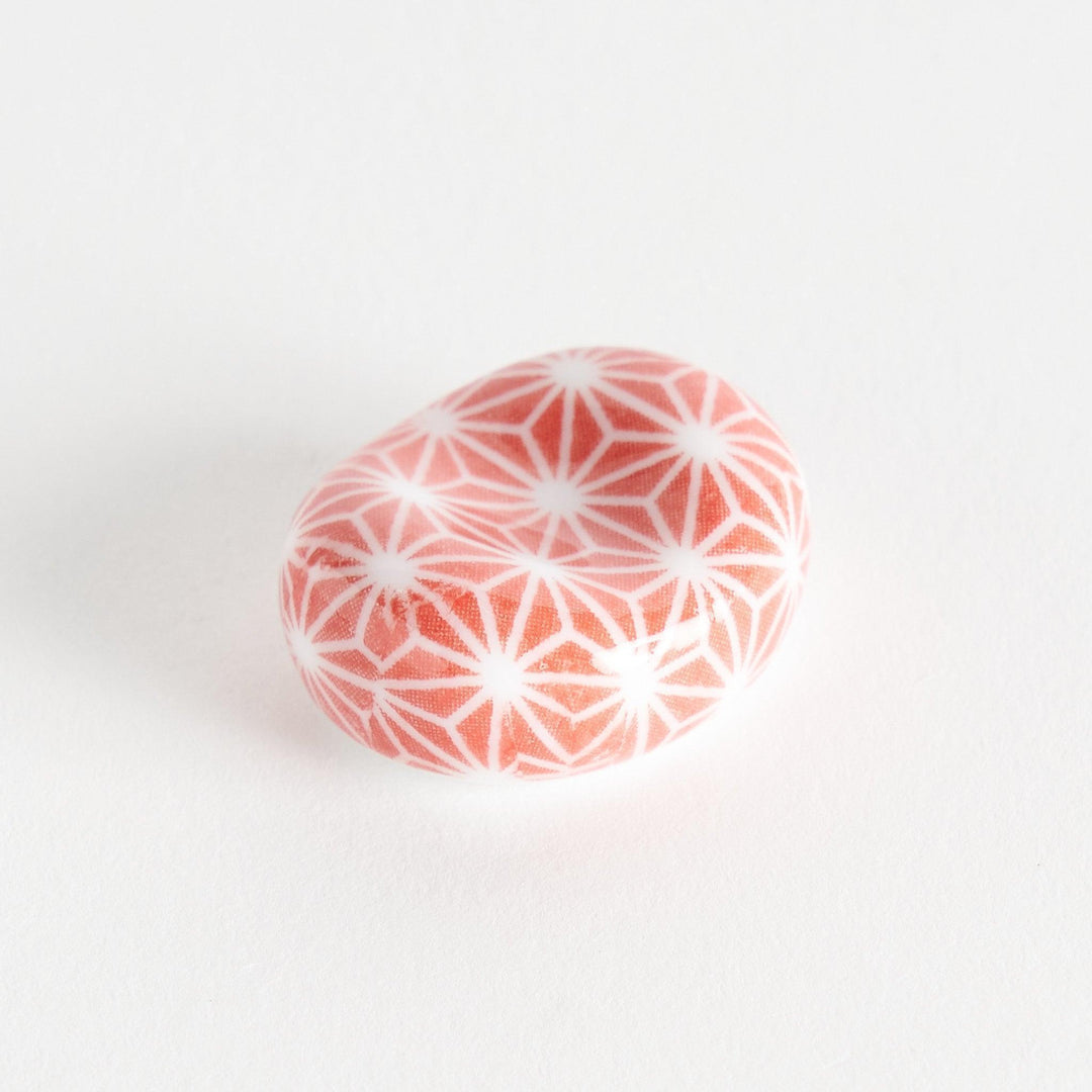 A red and white rounded ceramic chopstick rest with a starburst pattern.