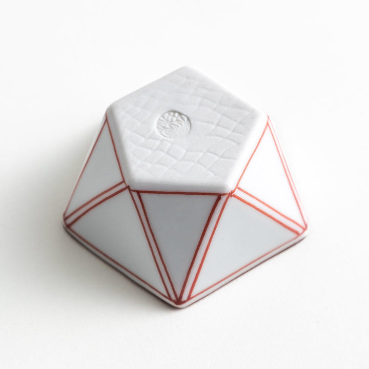 A small, white pentagonal bowl featuring red geometric lines and a brown rim.