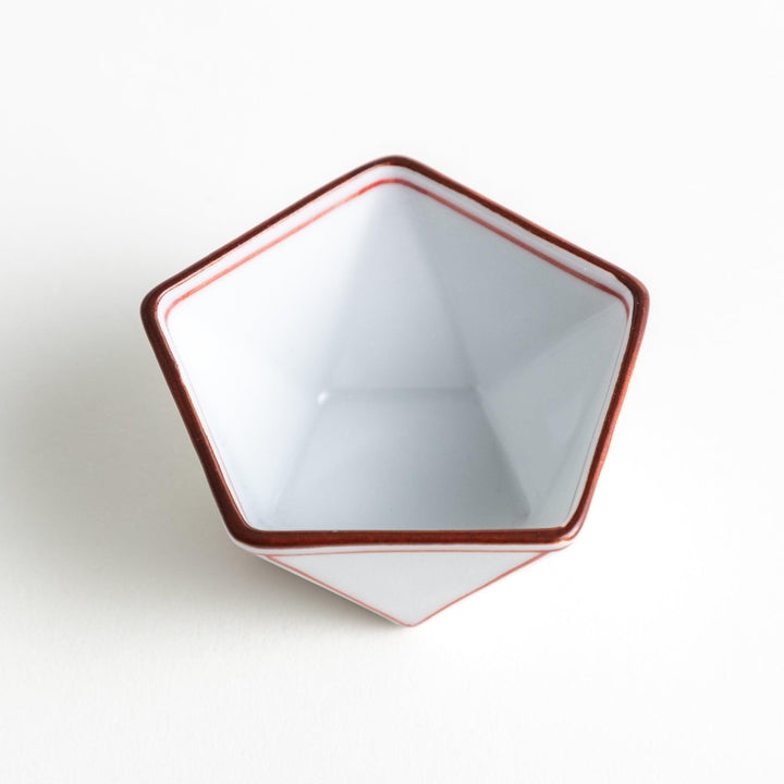 A small, white pentagonal bowl featuring red geometric lines and a brown rim.