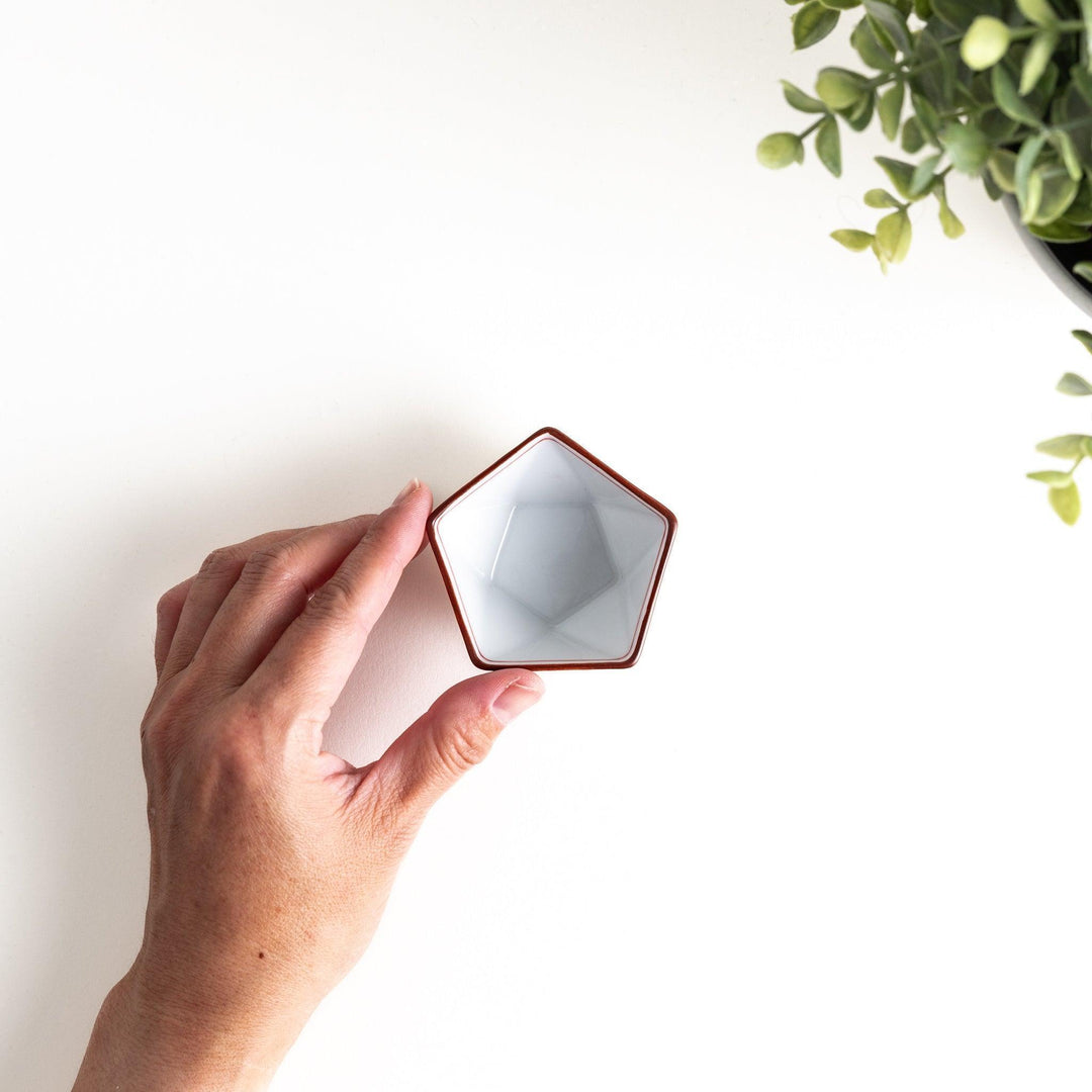 A small, white pentagonal bowl featuring red geometric lines and a brown rim.