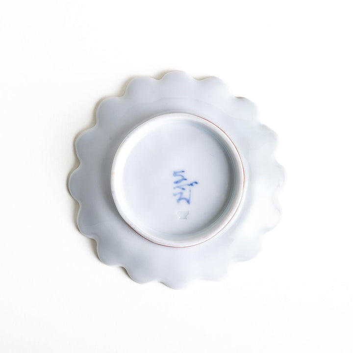 A small, scalloped-edge porcelain dish with orange chrysanthemum petal designs and a geometric center.