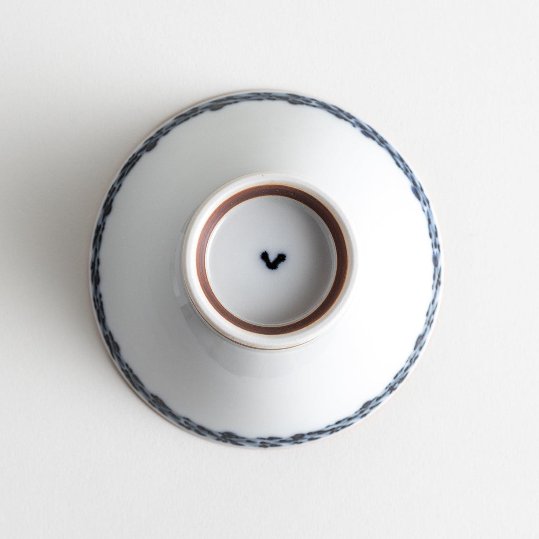 A white ceramic bowl decorated with a blue floral pattern around the rim and a brown base.