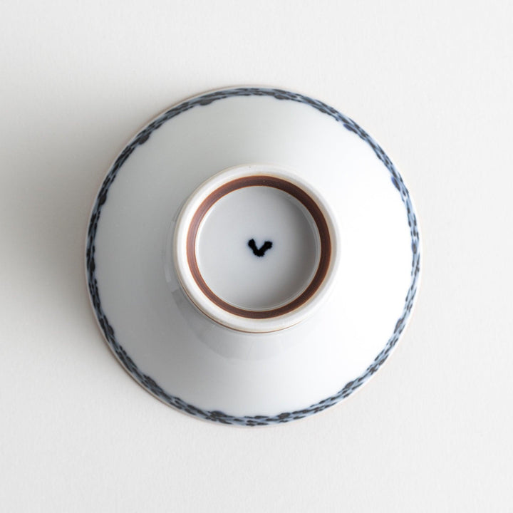 A white ceramic bowl decorated with a blue floral pattern around the rim and a brown base.