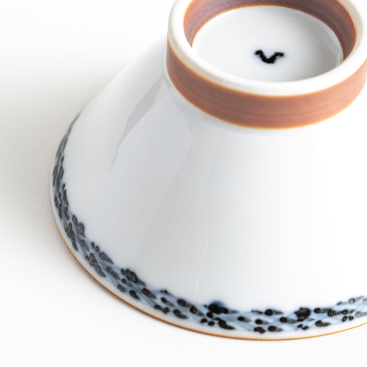 A white ceramic bowl decorated with a blue floral pattern around the rim and a brown base.