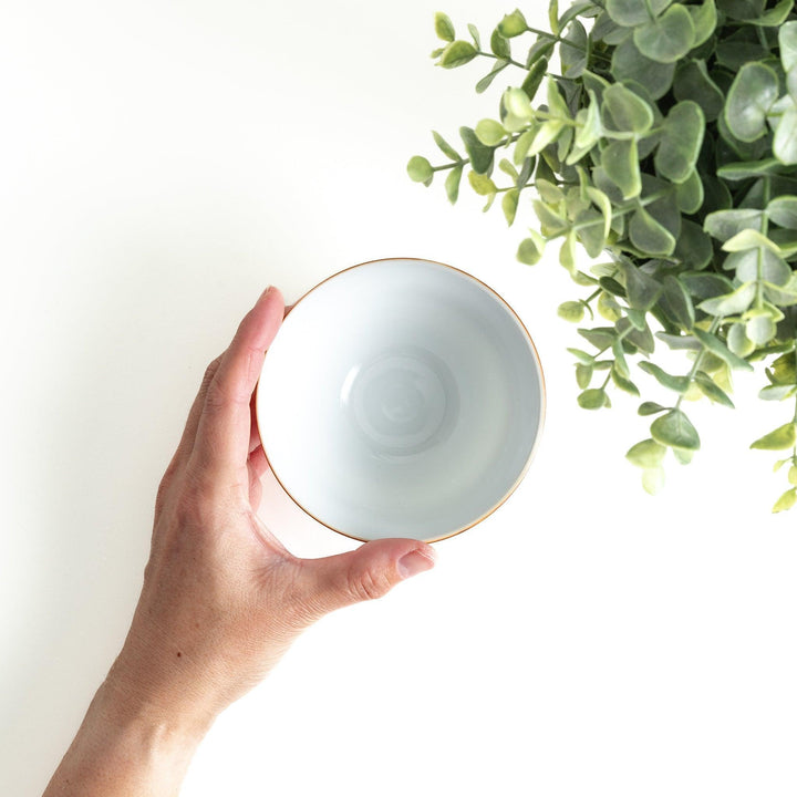 A white ceramic bowl decorated with a blue floral pattern around the rim and a brown base.