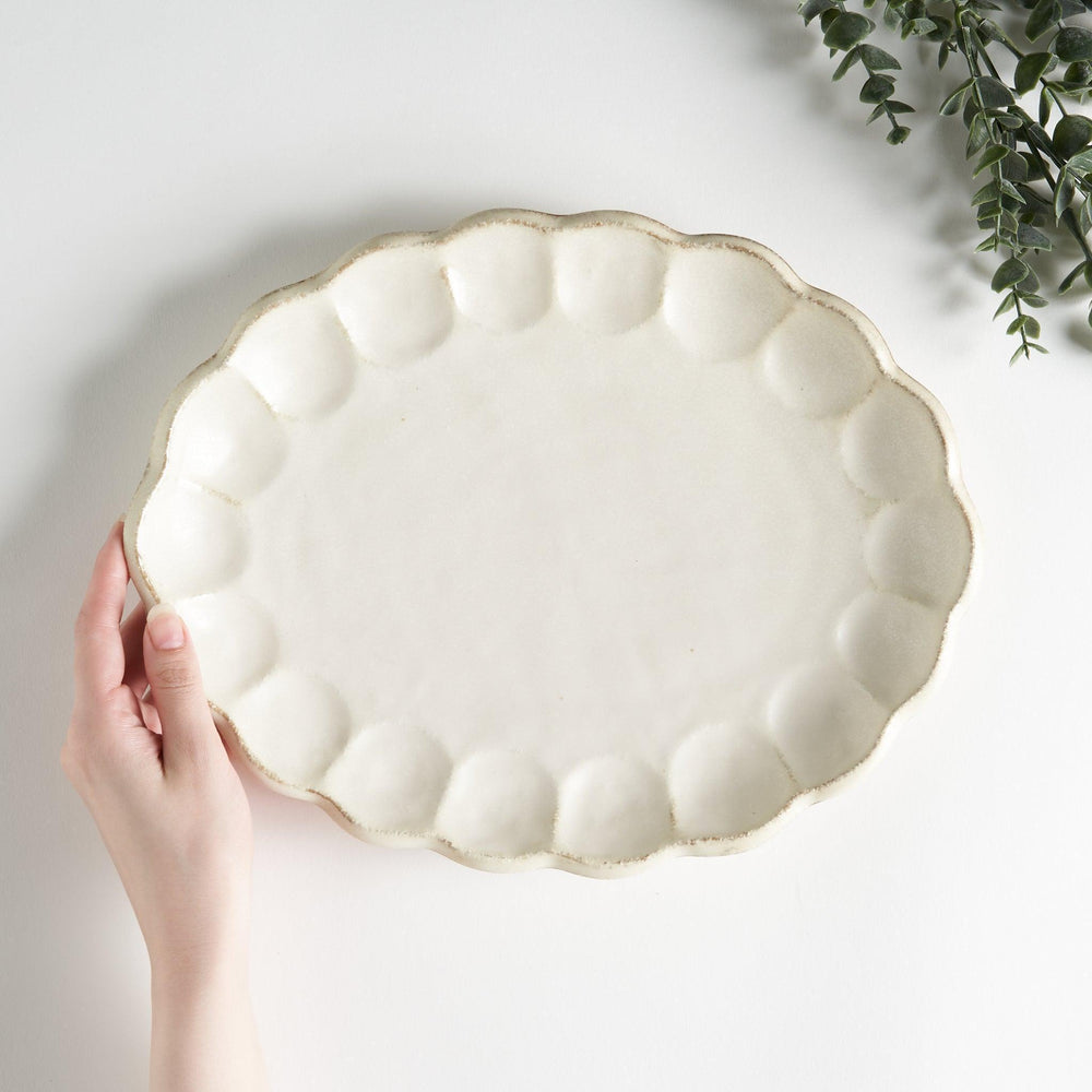 A white ceramic serving plate with a delicate, scalloped oval shape. Available in black or white.