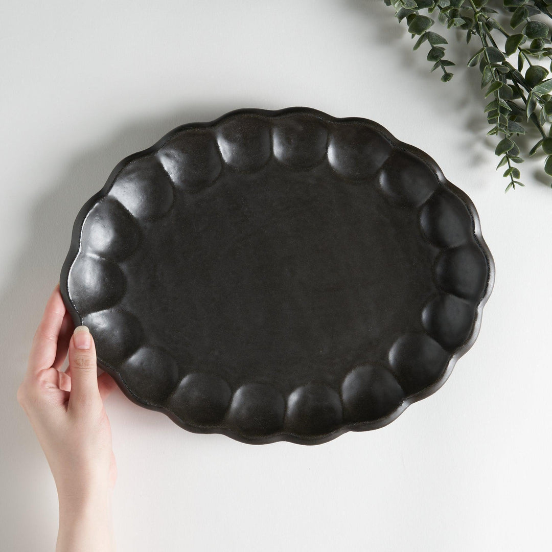 A white ceramic serving plate with a delicate, scalloped oval shape. Available in black or white.