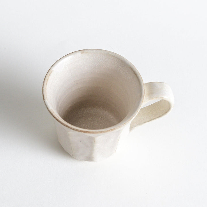 A minimalist ceramic mug with a textured, faceted finish. Available in black or white.