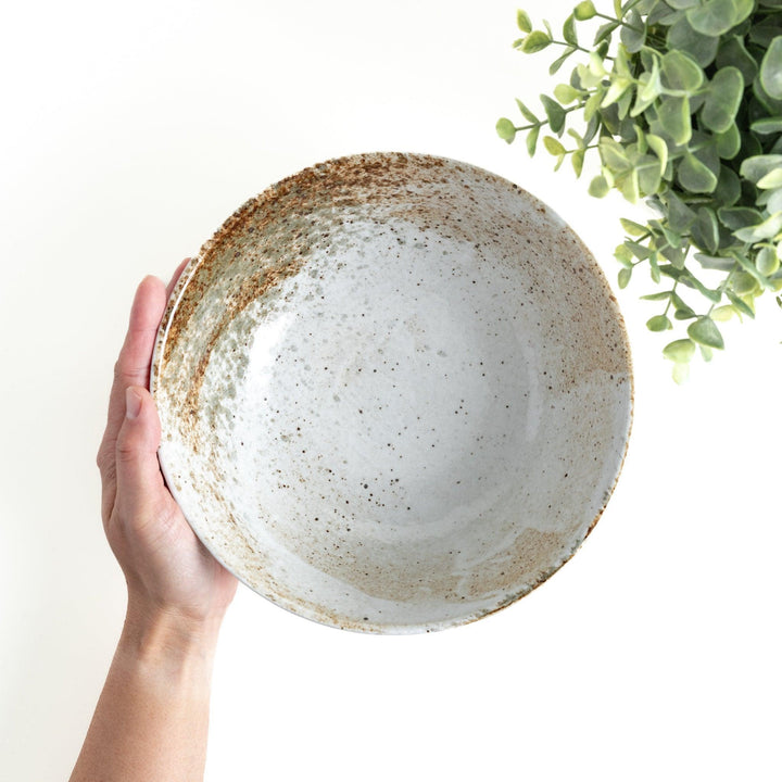 A large bowl with a speckled cream and brown glaze, featuring an organic, earthy design.